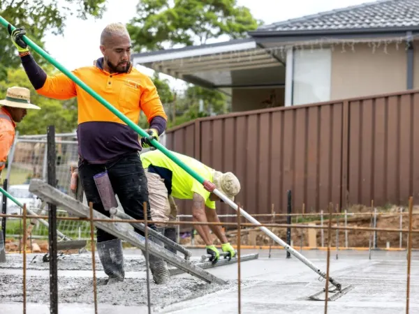 Two finishers screeding a freshly poured concrete slab next to a house
